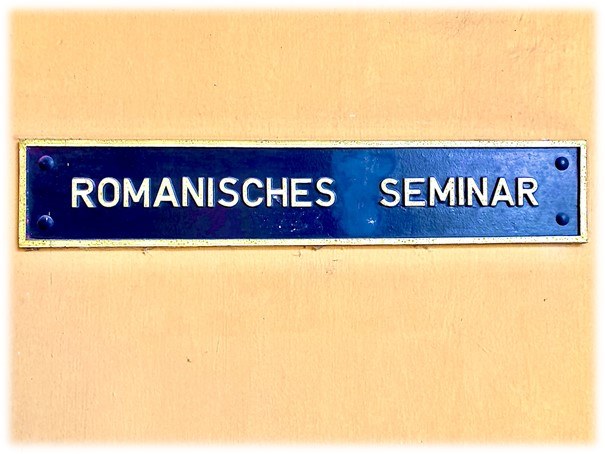 Eine Wissenschaftlerin und ein Wissenschaftler arbeiten hinter einer Glasfassade und mischen Chemikalien mit Großgeräten.